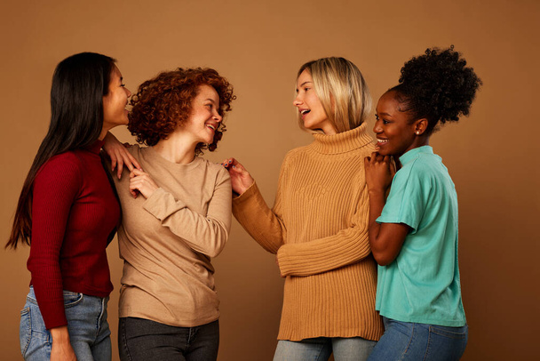 A multicultural female friends posing in studio isolated on brown background and chatting. - Foto, imagen