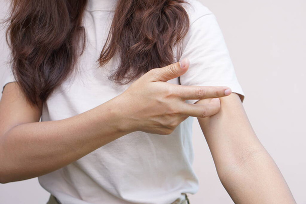 Woman scratching arm from itching on light gray background. Cause of itchy skin include insect bitesConcept of health care skin. - Foto, Imagen