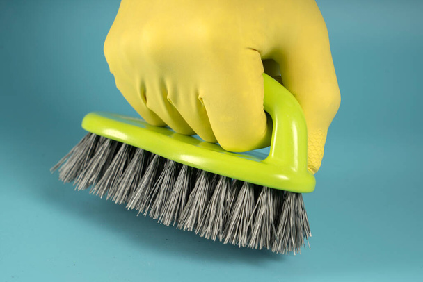 Mão em luva de borracha amarela detém esponja para lavar pratos e limpeza, mão aperta esponja no punho no fundo azul - Foto, Imagem