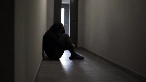 Silhouette of a depressed man sitting on the walkway of an apartment building. Sad man, crying, drama, lonely and unhappy concept. - Video