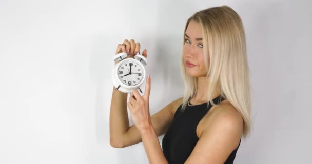 An attractive blonde haired woman holding up an old style alarm clock that is set to 8 o'clock, waking up at 8am or 8pm concept, filmed in 8k footage quality. - Video, Çekim
