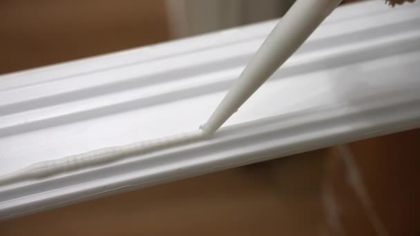 Process of applying glue on white baseboard surface with industrial tube, white sealant for plinth installing on construction site, using adhesive materials for home improvements. High quality 4k - Séquence, vidéo