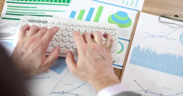 Manager tippt auf der Tastatur mit Finanzdiagrammen auf dem Tisch. Online-Bericht über kommerzielle Finanzindikatoren - Filmmaterial, Video