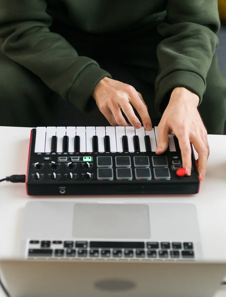 Запись электронной музыкальной дорожки с портативной миди-клавиатурой на ноутбуке в домашней студии. Производство и микширование музыки, создание ритмов и аранжировка аудио контента с профессиональными аудиоустройствами - Фото, изображение
