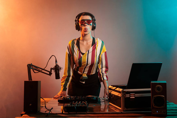 Female artist sticking tongue out and being funky, acting silly and fooling around over studio background. Confident cool DJ using turntables and audio equipment, mixing music. - Foto, immagini