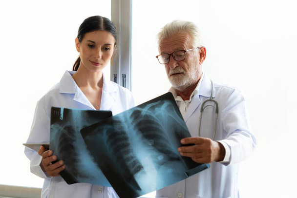 En una sala estéril del hospital, dos radiografos profesionales sostienen y examinan una radiografía para el diagnóstico médico de rayos X. El médico novato busca consejo sobre una condición de los pacientes de un médico experimentado. - Foto, imagen