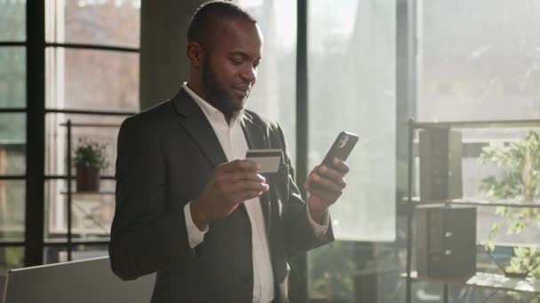 Ώριμος επιχειρηματίας African American 40s μεσήλικας σταθεί στο γραφείο χρήση κινητό τηλέφωνο πιστωτική κάρτα αγορά online πληρωμή στο ηλεκτρονικό κατάστημα pay banking εισάγετε κωδικούς αριθμούς εύκολη μεταφορά χρημάτων - Πλάνα, βίντεο