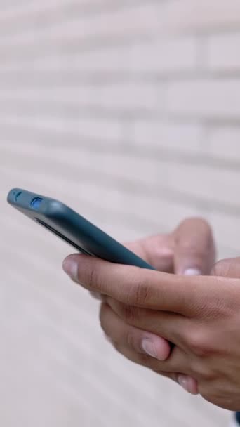 Вертикальне відео: крупним планом молодий афроамериканський чоловік, що використовує мобільний телефон на відкритому повітрі - Міленіум хлопець спілкується руками на смартфоні, спираючись на стіну
 - Кадри, відео