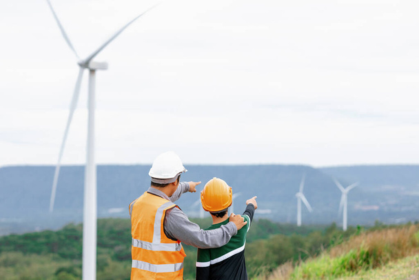 田舎の丘や山の上の風力発電所で彼の息子とエンジニア。再生可能エネルギー、持続可能なエネルギーの将来の生産のための進歩的な理想。風力タービンからの発電. - 写真・画像