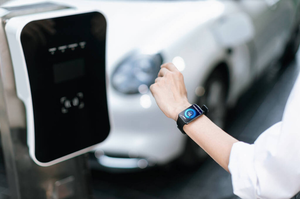 Крупним планом прогресивні годинники, що носяться, показують стан акумулятора електричного автомобіля, який заряджається в точці заряджання в місті. Цифровий інтерфейс, дані з дисплея автомобіля EV на смарт-годиннику
. - Фото, зображення