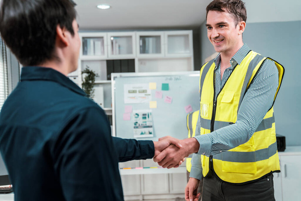 An engineer with a protective vest handshake with an investor in his office. Following a successful meeting, employee and employer form a partnership. - Foto, immagini