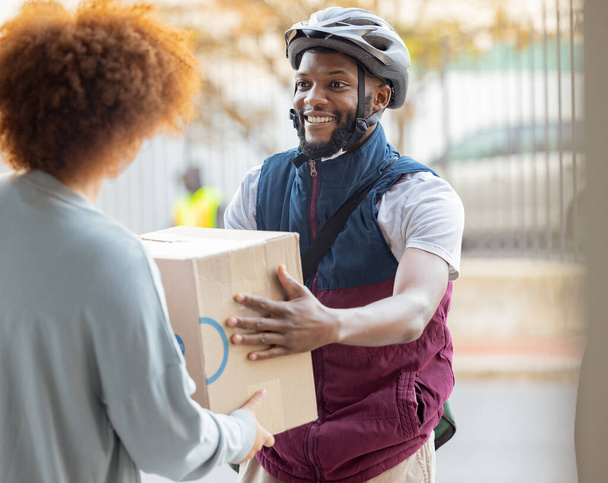 Black man, smile and delivery with box for woman at house for logistics, cargo and safety. Young african courier, package and shipping service with stock, helmet and e commerce job in neighborhood. - Photo, Image