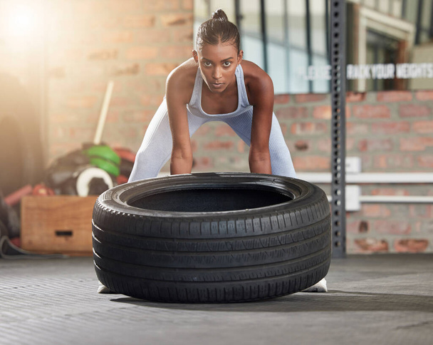 Exercise, fitness and portrait of woman with tire at gym for health and wellness with training workout. Indian athlete person focus on hard work and commitment to train for strong body goals or power. - Photo, Image