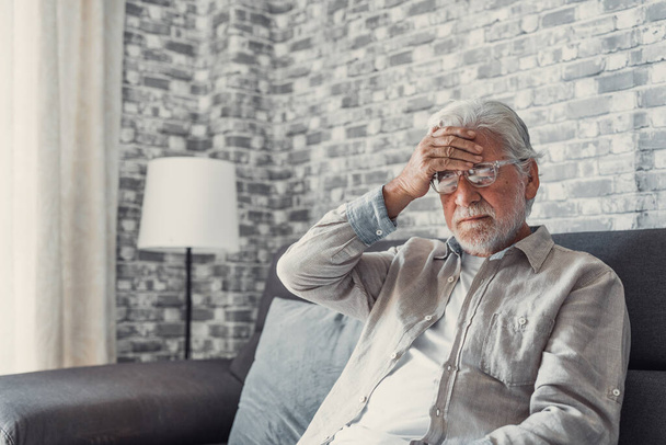 Frusztrált, egészségtelen, idős férfi megérinti a fejét, fájdalmas érzései vannak otthon ülve. Boldogtalan középkorú nyugdíjas nagyapa szenved magas vérnyomás betegség beltéri. - Fotó, kép