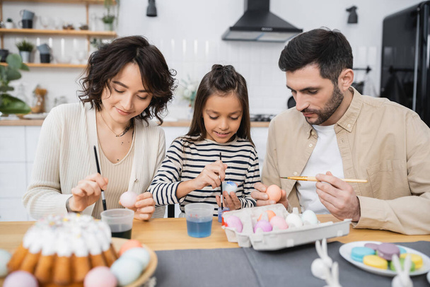 Peinture de famille oeufs de Pâques près de gâteau flou sur la table dans la cuisine  - Photo, image
