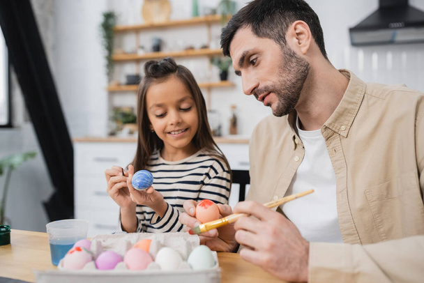 father and happy daughter coloring Easter eggs in kitchen   - Photo, image
