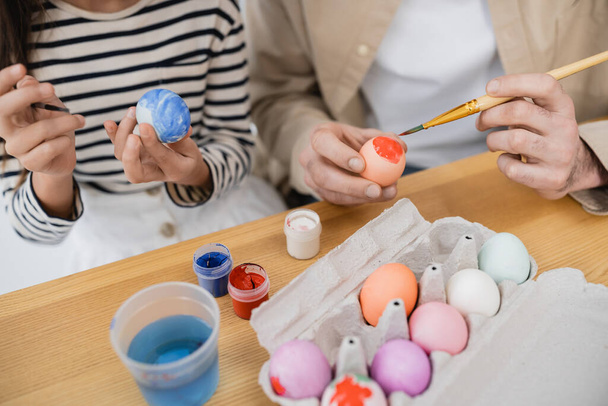 Καλλιεργημένη άποψη του κοριτσιού και του μπαμπά χρωματισμός πασχαλινά αυγά στο σπίτι  - Φωτογραφία, εικόνα