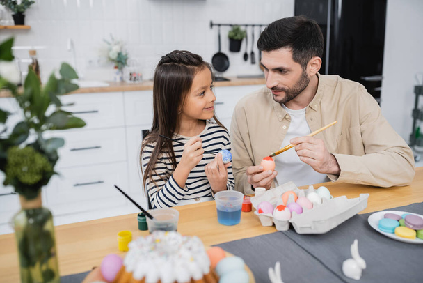 Férfi beszél a lányával, miközben a húsvéti tojásokat festi a konyhában  - Fotó, kép
