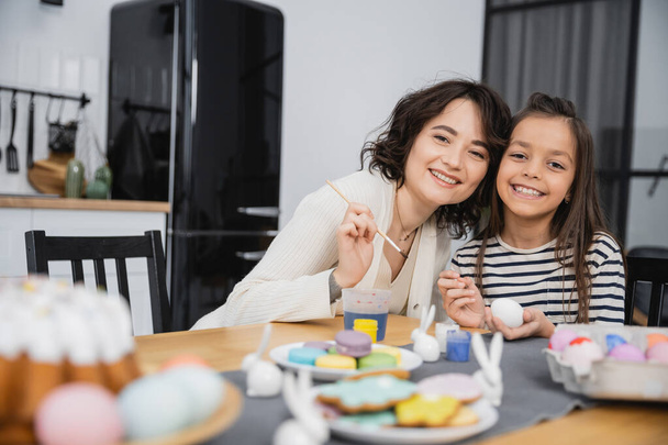 Mother and daughter looking at camera while coloring Easter eggs at home  - Photo, Image