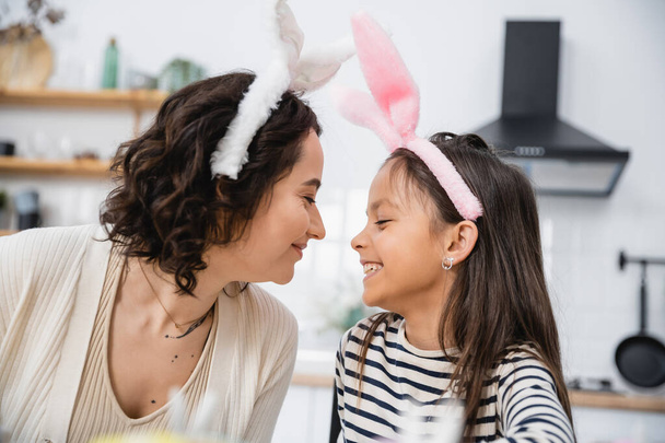 Side view of smiling mom and daughter in Easter headbands at home  - Fotó, kép