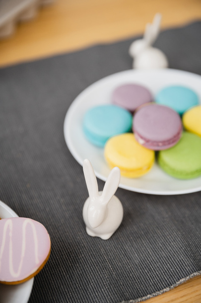 Figurine de lapin de Pâques près de macarons colorés sur la table à la maison  - Photo, image