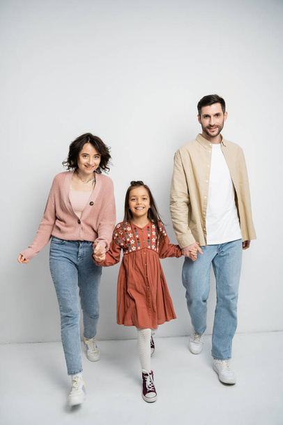 Positive family holding hands and walking on white background  - Zdjęcie, obraz