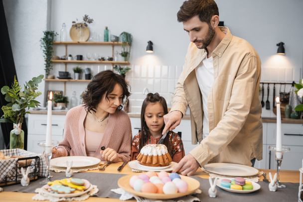 Father cutting Easter cake near daughter and wife during festive dinner  - 写真・画像