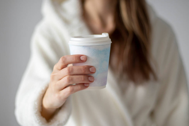 A woman holding a plastic coffee cup with a delicate watercolor drawing in her hand at home. - 写真・画像