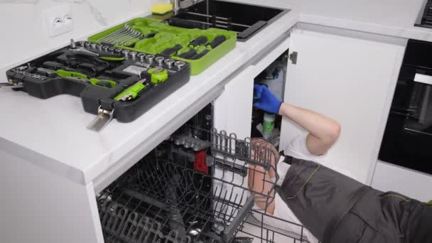 Τεχνίτης κατά την εγκατάσταση πλυντηρίου πιάτων. Εγκατάσταση οικιακών συσκευών στο χώρο της κουζίνας. Βίντεο 4k - Πλάνα, βίντεο