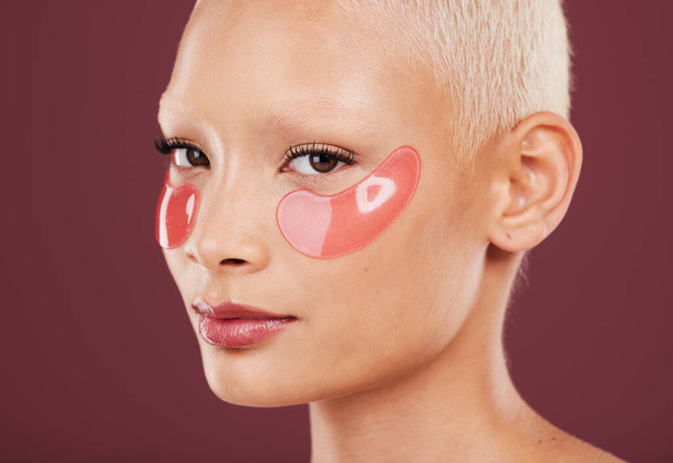 Portrait, eye mask and skincare with a model black woman in studio on a red background for beauty. Face, skin and antiaging with an attractive young female posing to promote a cosmetic product. - 写真・画像