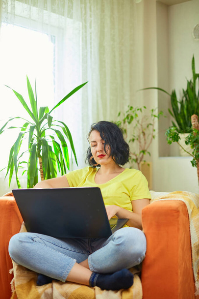 Mujer femenina usando tecleando en el teclado del ordenador portátil, trabajando, escribiendo correos electrónicos, freelancer trabajando en portátil en casa sentado en el sillón naranja casa verde. - Foto, Imagen