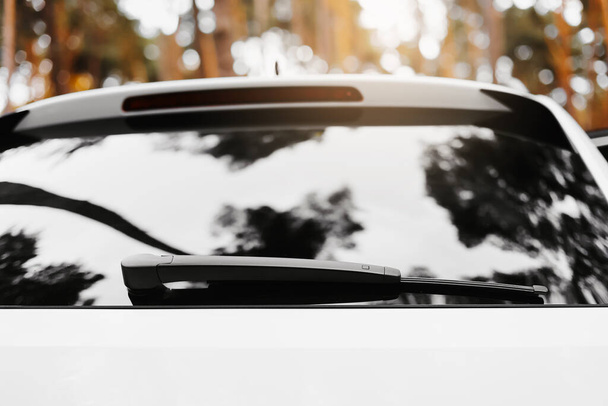 Отражение деревьев и неба в задней части окна припаркованной белой машины. Дворники ветрового стекла - Фото, изображение