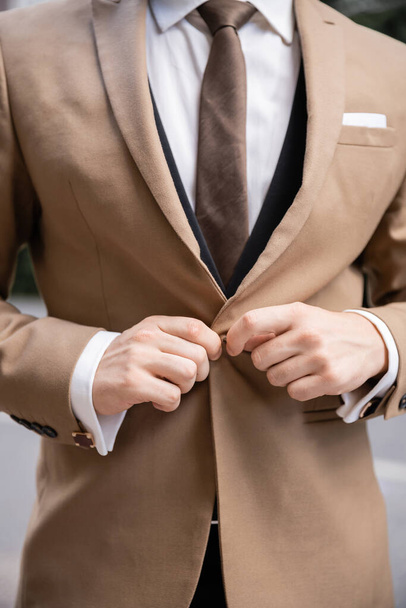cropped view of man in white shirt with tie buttoning beige blazer  - Fotografie, Obrázek