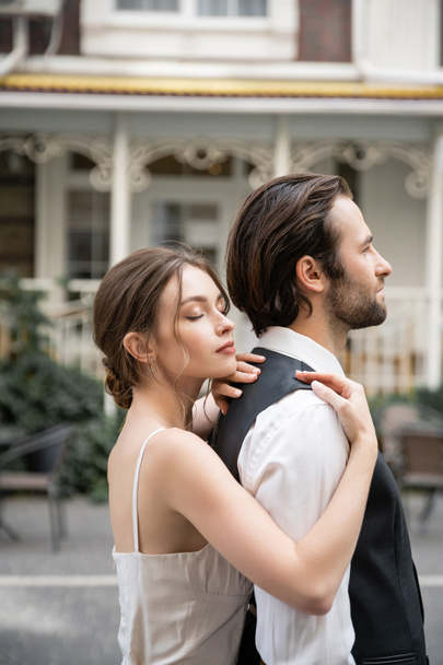 young bride in wedding dress standing with closed eyes and hugging groom in vest  - Foto, Bild