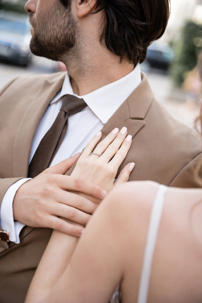 ostříhaný pohled na mladou ženu se snubním prstenem na prstu stojící poblíž ženicha v obleku  - Fotografie, Obrázek