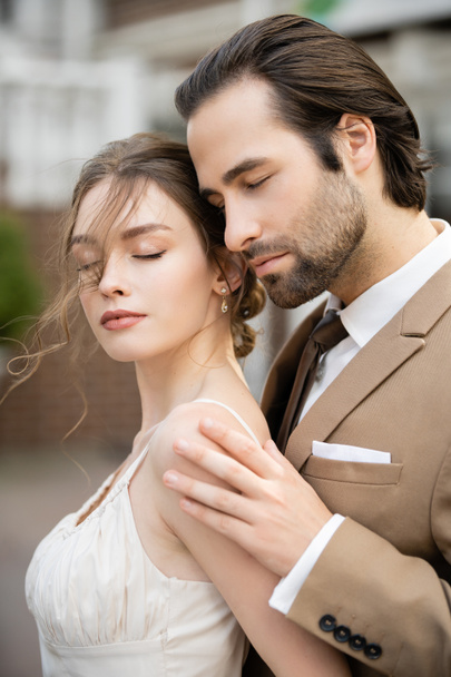 marié en blazer beige étreignant magnifique mariée en robe de mariée blanche  - Photo, image