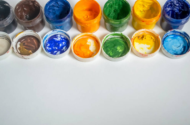 Jars of watercolor paint stand in a row. Color watercolor with open lids on a white background. A number of watercolors. - 写真・画像