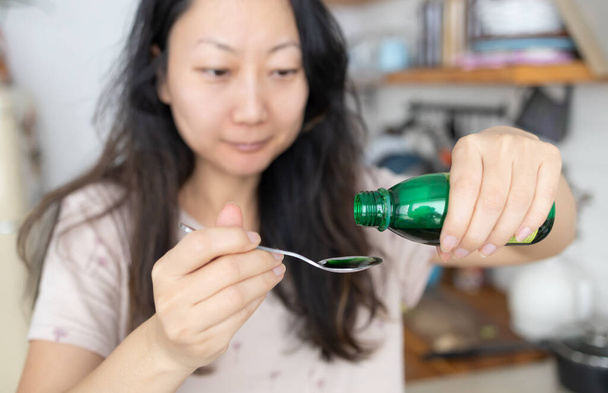 медицинское обслуживание, люди и медицинская концепция - азиатская женщина наливает лекарства или антипиретический сироп из бутылки в ложку - Фото, изображение