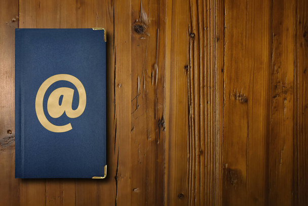Großaufnahme auf dunkelblauem Adressbuch mit vergoldetem At-Schild in der Mitte. - Foto, Bild