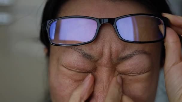 疲れてアジアの女性は、夜にリビングルームで眼鏡を保持彼女の鼻の橋をマッサージ。若いOLは目を傷つける痛みを発散させるために首を振り続ける。いらいらするストレスの多い女性. - 映像、動画