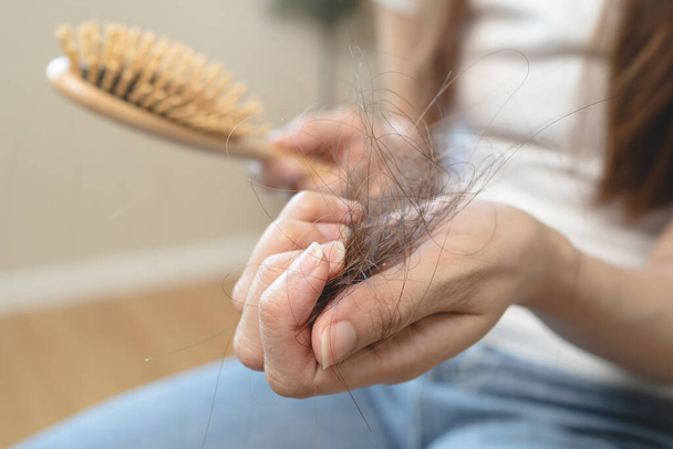 Haarausfall-Problemkonzept. Schockierte Asiatin blickt auf viele Haare, die sie in der Hand und im Kamm verloren hat. - Foto, Bild