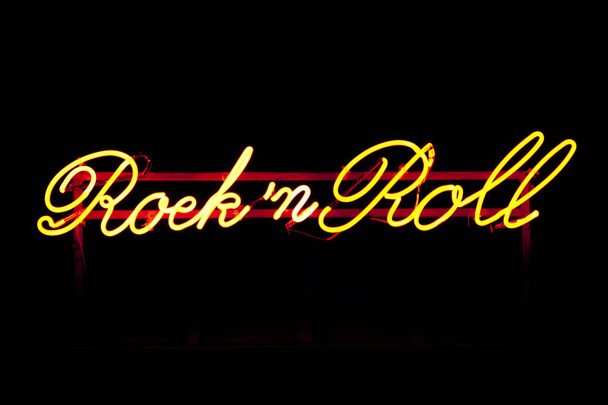 Close-up on a yellow neon light shaped into the phrase "Rock n Roll". - Valokuva, kuva