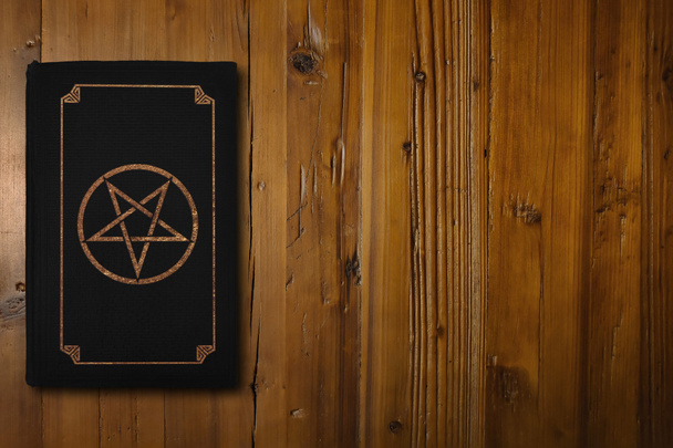 Kahverengi bir tahtanın üzerinde yaldızlı bir Pentagram olan siyah bir kitaba yakın plan.. - Fotoğraf, Görsel