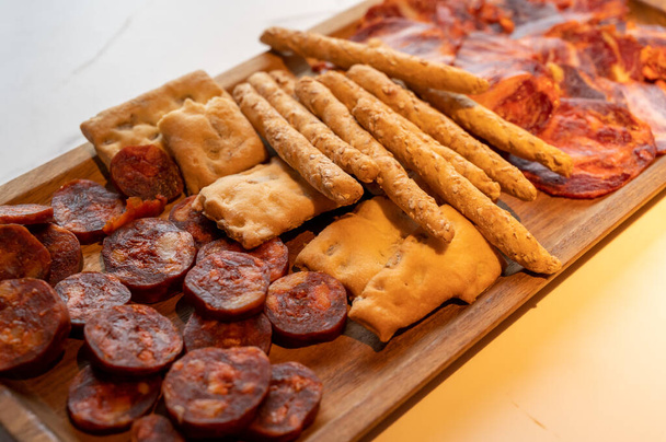 Piatto di legno con tapas spagnole affettate, salsiccia choriso, lomo iberico en bread sticks, primo piano - Foto, immagini