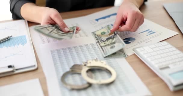 Person counts cash money dollar with business charts and handcuffs on table. Corruption Bribery and tax evasion - Felvétel, videó