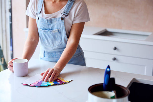 Primer plano de la mujer renovando la cocina en casa mirando muestras de pintura en el descanso de café - Foto, Imagen