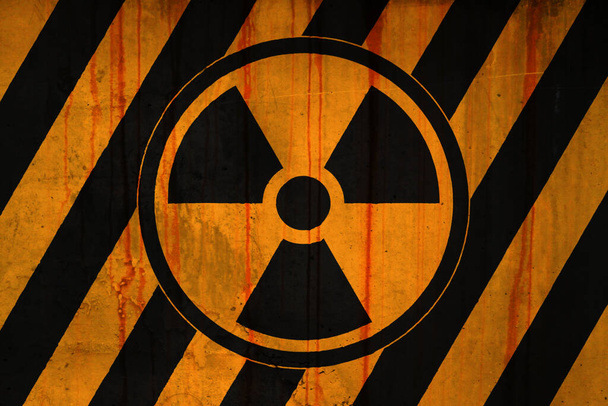 Full-frame weathered concrete wall covered with rust stains and paint in yellow and black stripe with a radioactive symbol. - Foto, imagen