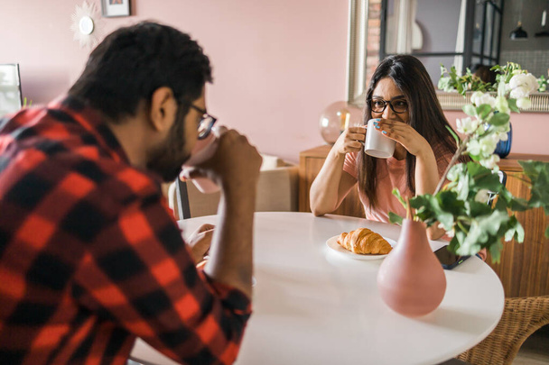 Szczęśliwa para je śniadanie i rozmawia rano przy stole. Indianka i Latynos. Związek i różnorodność - Zdjęcie, obraz