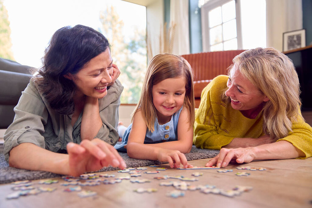 Same Sex Family With Two Mature Mums And Daughter Lying On Floor Doing Jigsaw Puzzle At Home - Fotografie, Obrázek