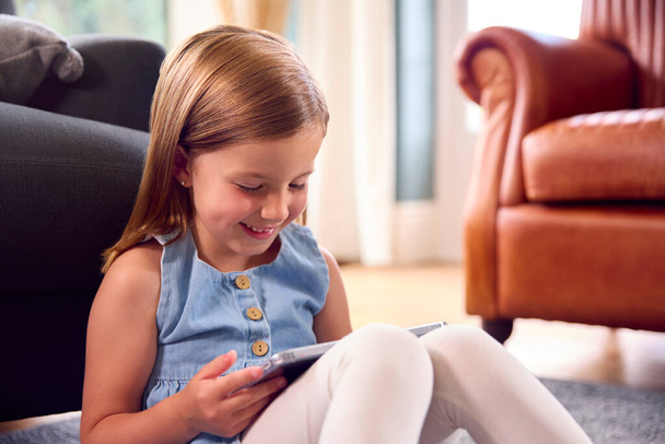 Young Girl At Home Sitting On Floor Of Lounge Playing Game Or Watching Movie On Digital Tablet - Фото, зображення